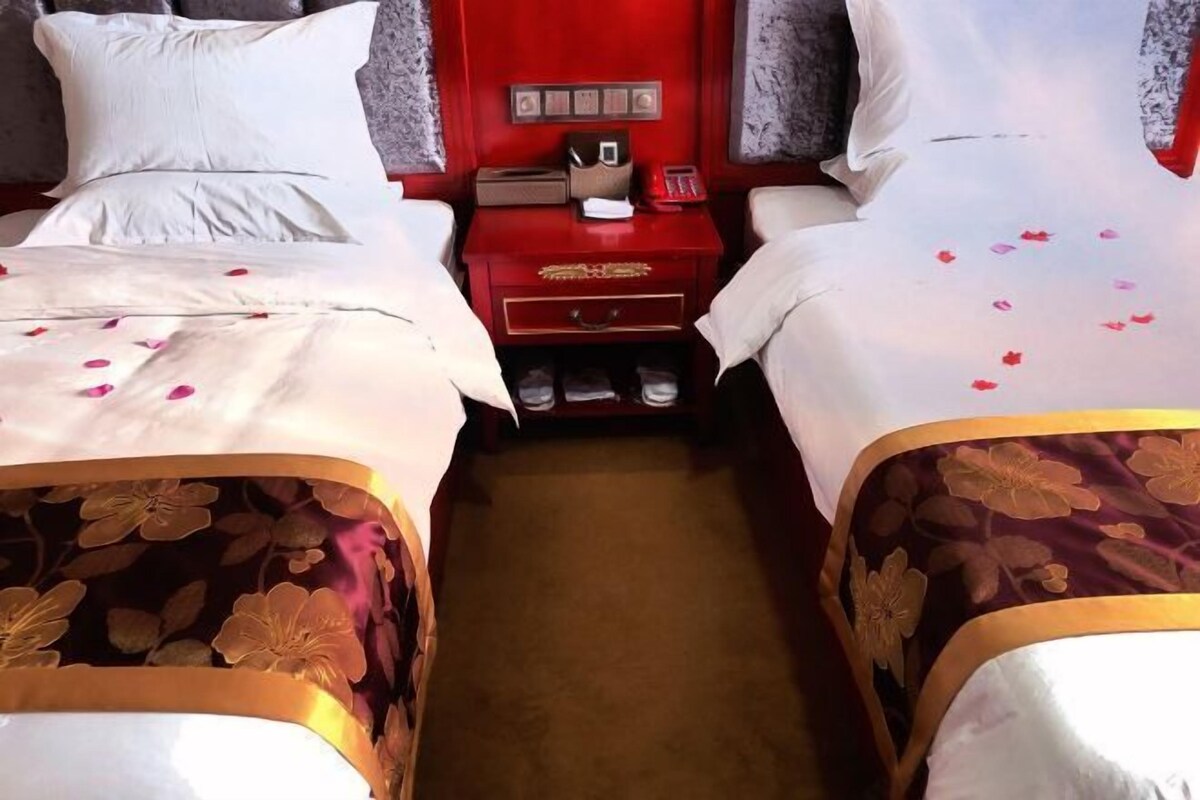 A hotel room with two beds, a red nightstand with a phone and a small box, and a carpeted floor.
