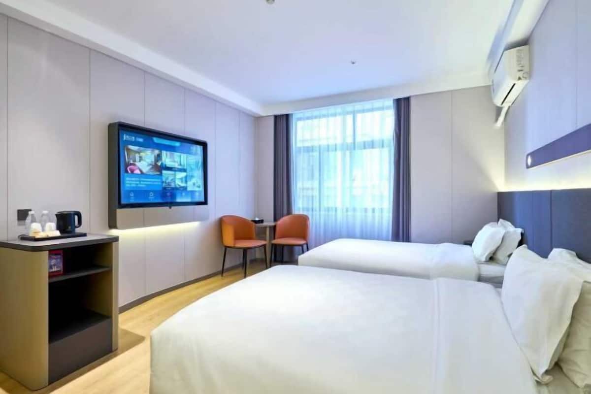 A hotel room with a bed, a TV, a desk with a chair, and a window.