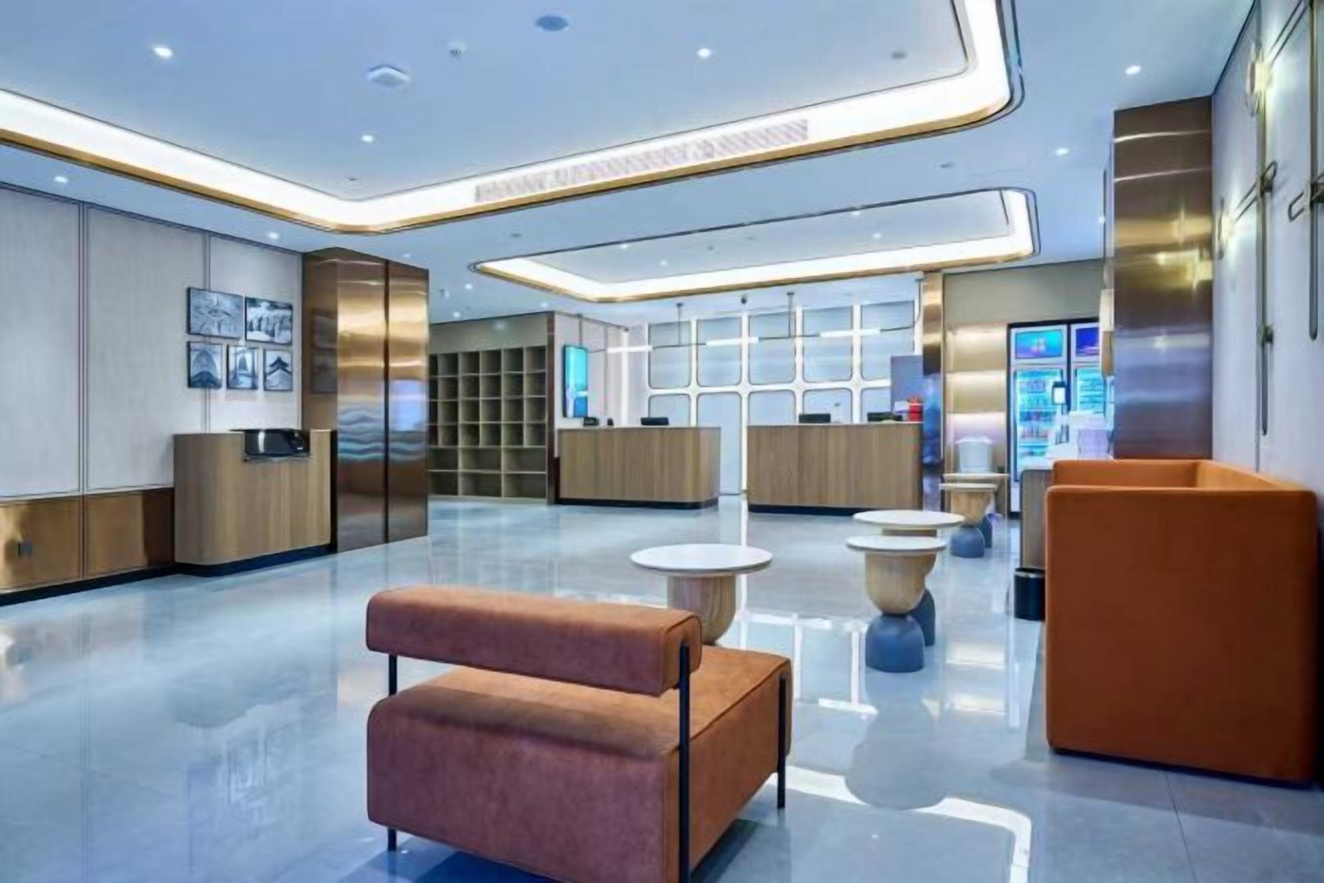 A modern lobby with a reception desk, seating areas, and a digital information kiosk.