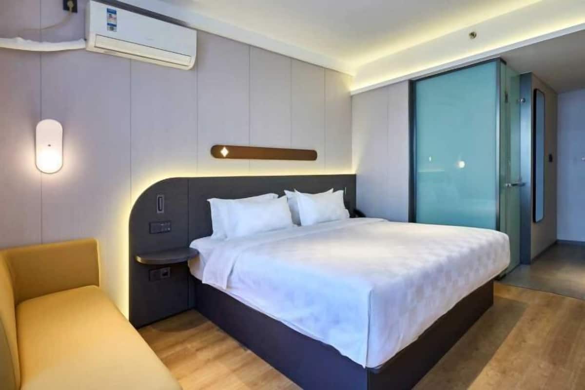 A modern hotel room with a large bed, bedside tables, a built-in heater, and a sliding door to a bathroom.