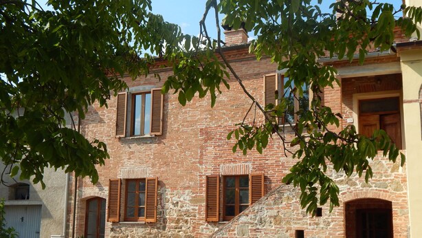 Un edificio tradicional de ladrillo con contraventanas de madera, una escalera de piedra y una puerta pequeña.
