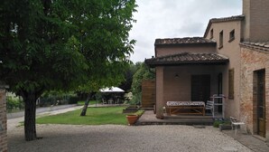 Un patio con suelo de grava, una mesa de madera con sillas, un edificio de ladrillo y un árbol.