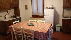 Una cocina compacta con armarios de madera, un refrigerador blanco, una mesa de comedor con mantel a cuadros y sillas blancas.