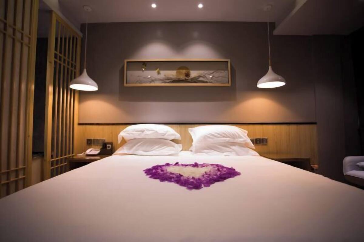 Ein Hotelzimmer mit einem großen Bett, zwei Nachttischen, einem Schranken und einem Gemälde über dem Bett, sowie einer Holzvertäfelung an einer Seite.
