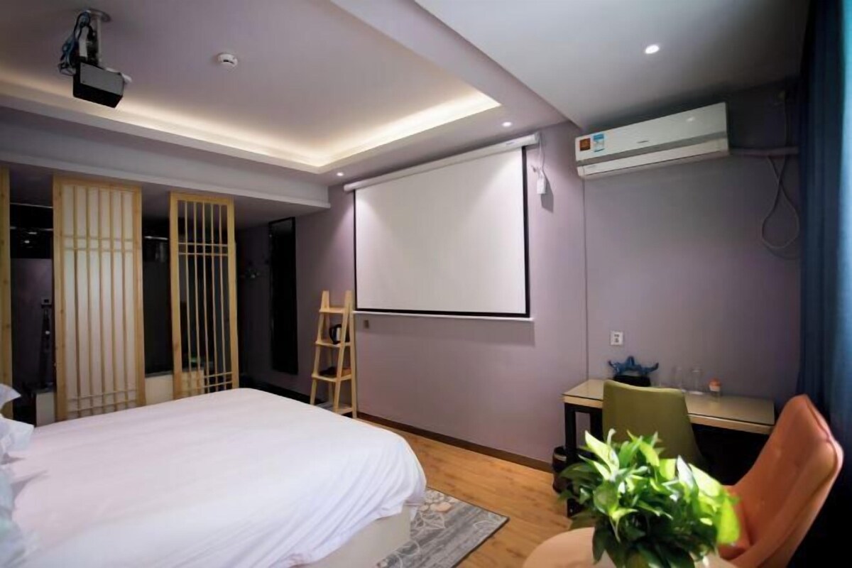 A modern hotel room with a bed, a desk, a projector, and an air conditioning unit.