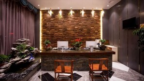 Een receptiezone met een houten wand, twee barkrukken, een receptiebalie, een flatscreen-televisie en een decoratieve plantenwand.