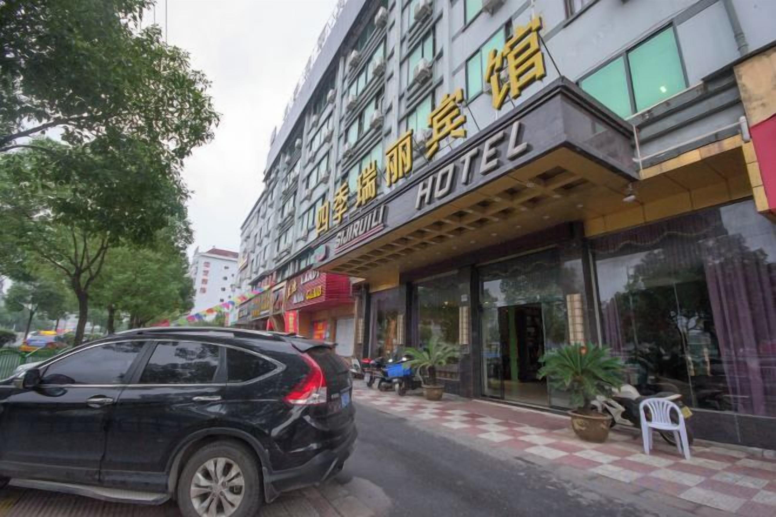 A hotel with a visible entrance, a parked car, and a potted plant outside.