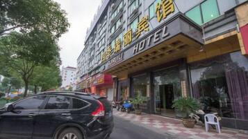 A hotel with a visible entrance, a parked car, and a potted plant outside.