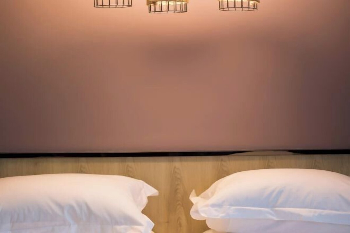 A hotel room with a wooden headboard, two white pillows, and three wall-mounted light fixtures.