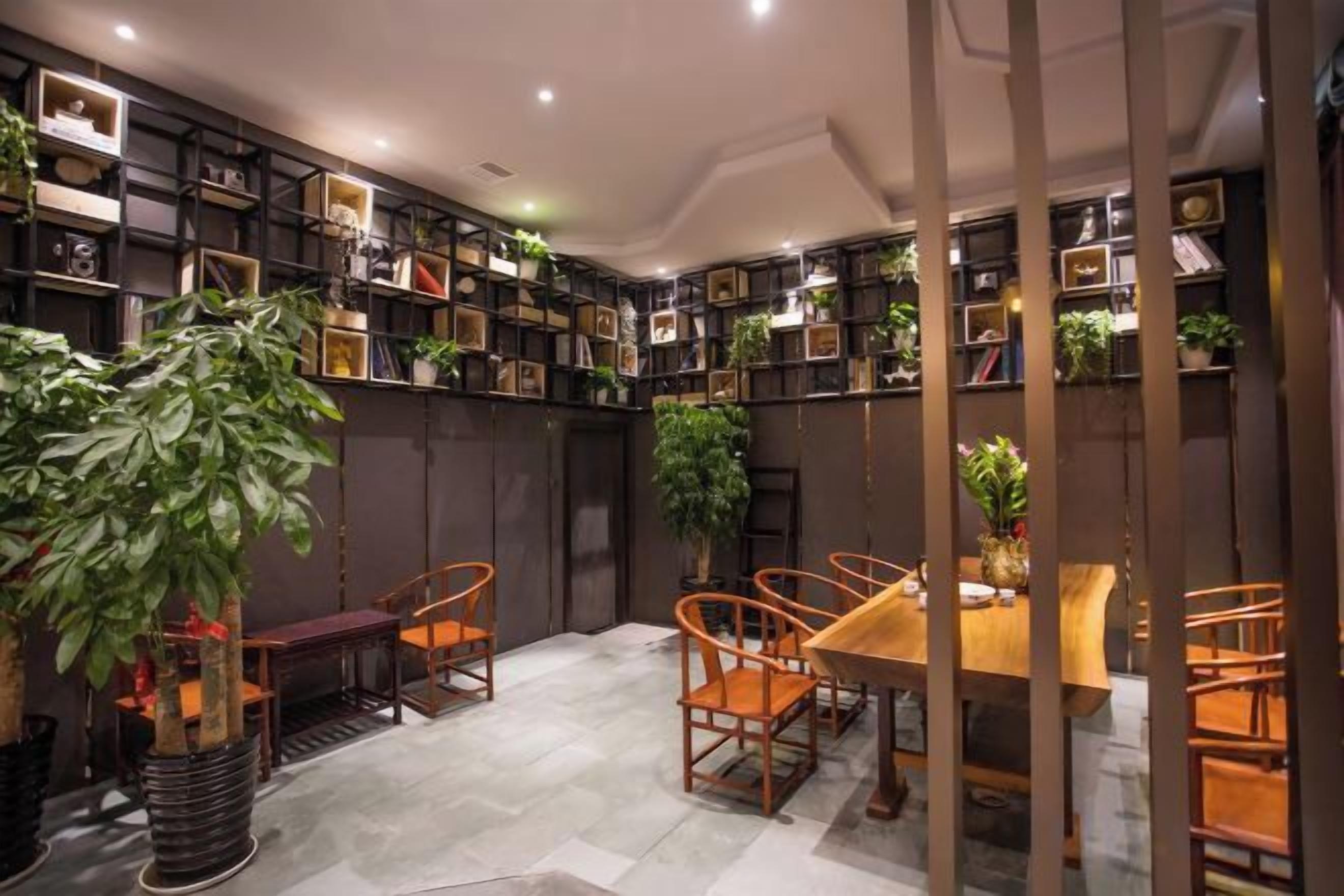 A room with a dining table, chairs, and shelves with books and plants.