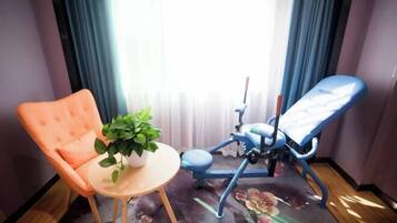 A room with a blue dental chair, an orange chair, a small round table with a potted plant, and a floral carpet.