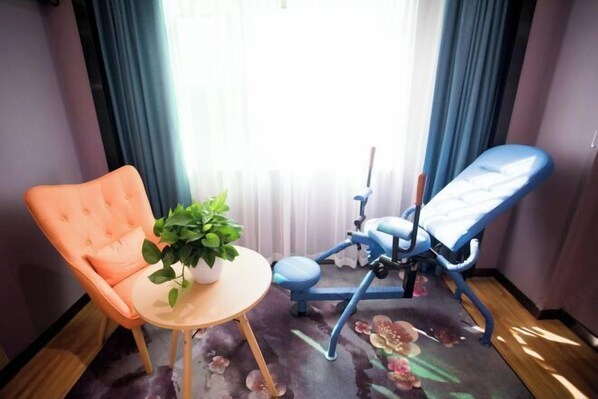 A room with a blue dental chair, an orange chair, a small round table with a potted plant, and a floral carpet. - Siji Ruili Hotel (Yiwu)