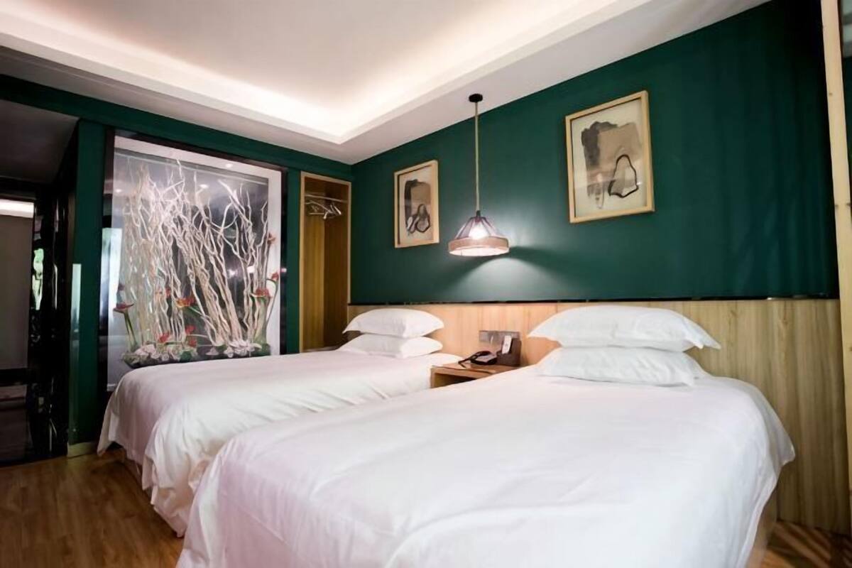 Ein Zimmer mit zwei Betten, einem hölzernen Kopfteil, einem Nachttisch, einer Pendelleuchte und einer grünen Wand.