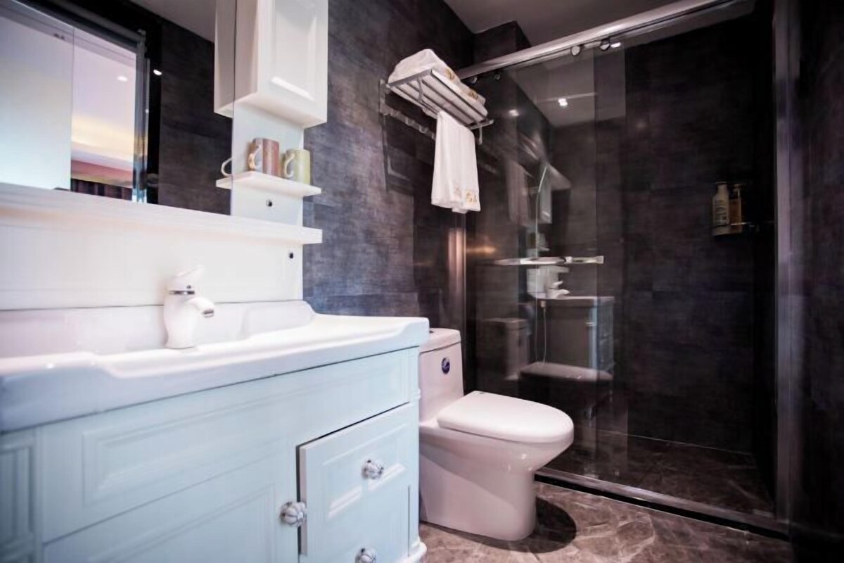 A modern bathroom with a white vanity, a glass shower enclosure, and a dark tiled wall.