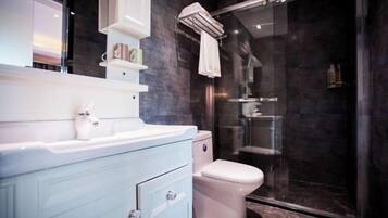 Un baño moderno con un tocador blanco, cabina de ducha con mampara de vidrio y pared revestida de baldosas oscuras.