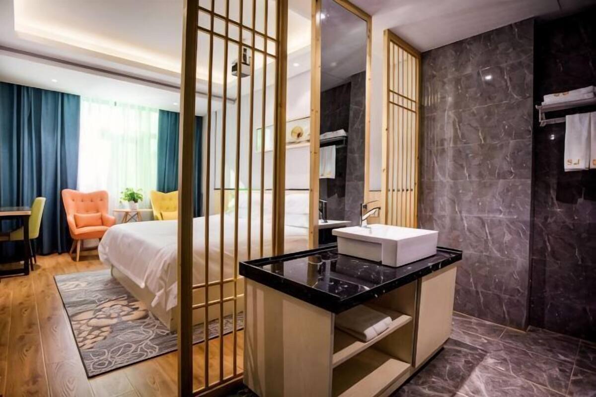 Ein modernes Hotelzimmer mit Bett, Badezimmer mit Waschbecken und Spiegel, Schreibtisch mit Stuhl und Blick ins Freie.