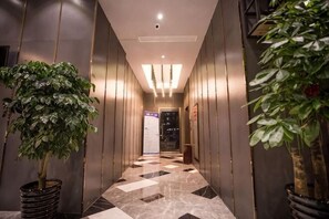 A hallway with a checkered floor, potted plants, and a door at the end. - Siji Ruili Hotel (Yiwu)