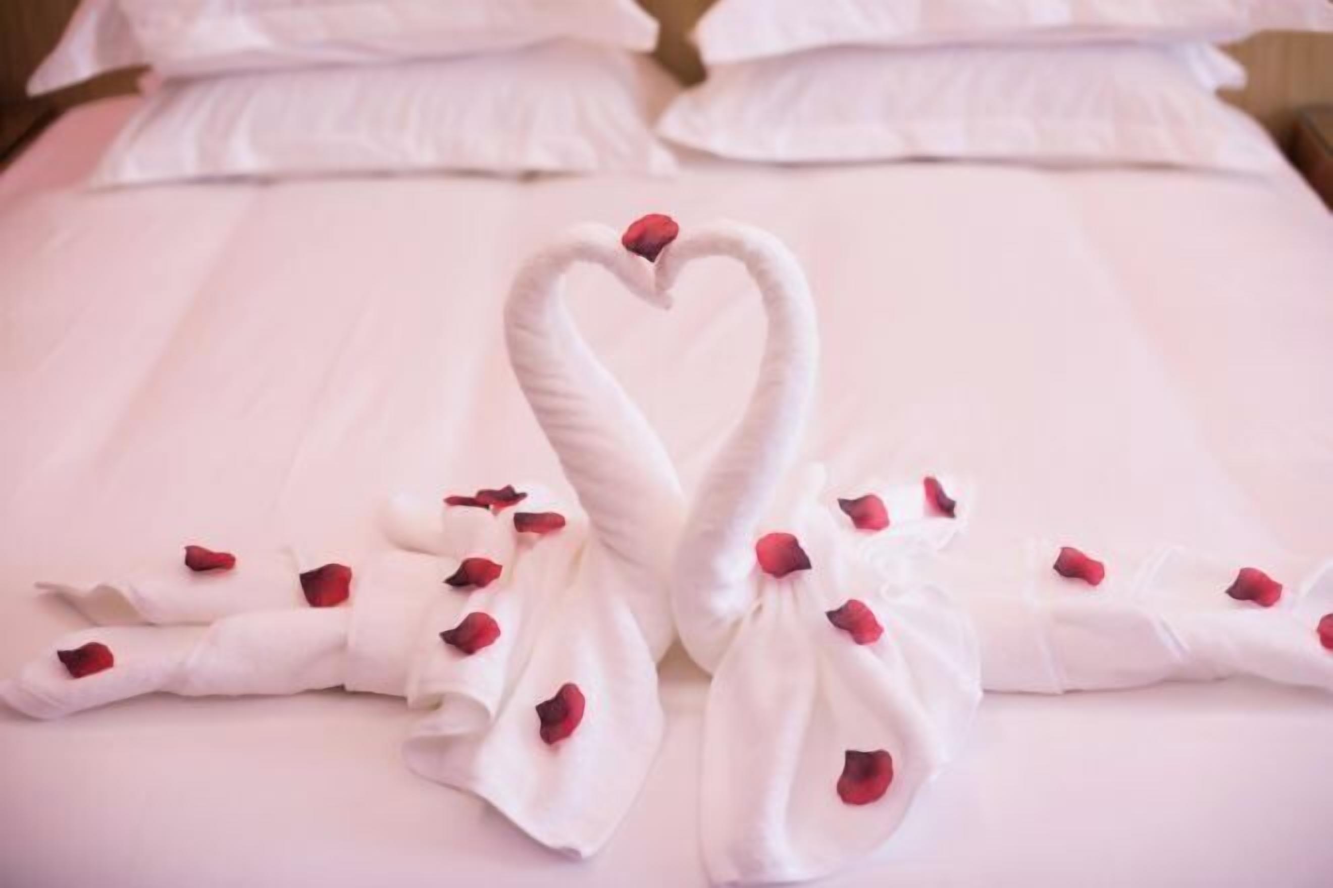 Una cama con toallas dispuestas en forma de corazón y pétalos de rosa.