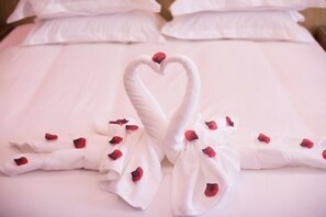 A bed with a heart-shaped towel arrangement and rose petals. - Siji Ruili Hotel (Yiwu)