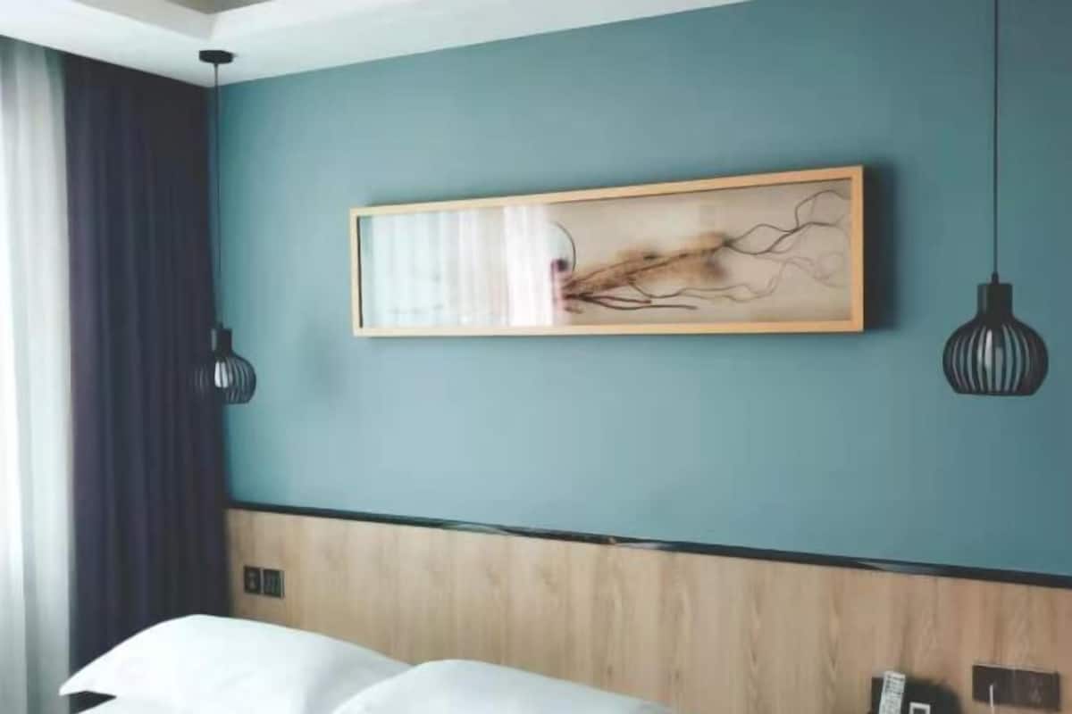 Ein Hotelzimmer mit einer türkisblauen Wand, einem hölzernen Kopfteil, einem Bett mit weißer Bettwäsche und einem gerahmten abstrakten Gemälde.