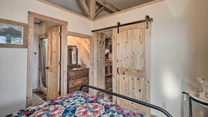 A bedroom with a bed, wooden wardrobe, and a bathroom visible through an open door. - Kerrville Converted Barn Tiny Home w/ Kayaks! (Kerrville)