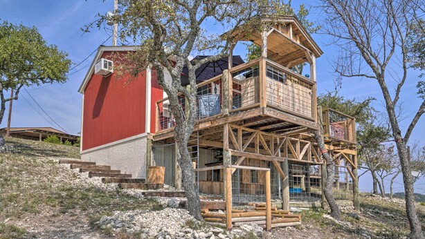 A wooden cabin with a red exterior, a balcony, and a staircase leading to the upper level. - Kerrville Converted Barn Tiny Home w/ Kayaks! (Kerrville)