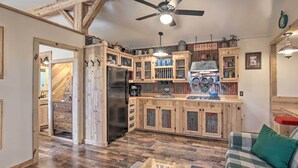 A rustic kitchen with wooden cabinets, a black refrigerator, and a ceiling fan. - Kerrville Converted Barn Tiny Home w/ Kayaks! (Kerrville)