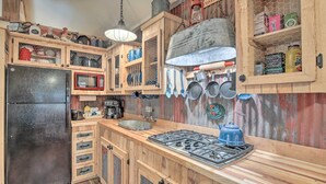A rustic kitchen with wooden cabinets, a black refrigerator, a stove, and various kitchen utensils and cookware. - Kerrville Converted Barn Tiny Home w/ Kayaks! (Kerrville)