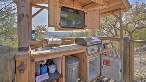 A wooden outdoor kitchen with a built-in TV, grill, and sink. - Kerrville Converted Barn Tiny Home w/ Kayaks! (Kerrville)