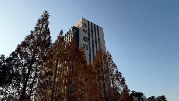A tall building with vertical lines, surrounded by trees. - Ji Hotel (Shanghai)