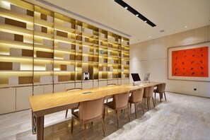 Una sala de conferencias moderna con una larga mesa, sillas, una estantería y un cuadro abstracto de gran tamaño.