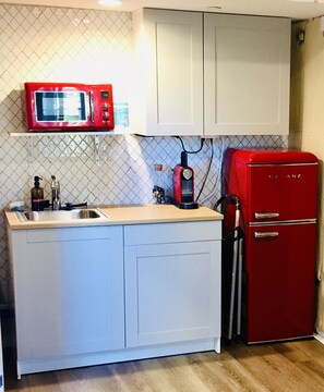 A compact kitchen with white cabinets, a red microwave, and a red refrigerator.