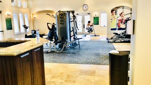 Een sportschool met diverse fitnessapparaten, een klok aan de muur en een balie met een spiegel.