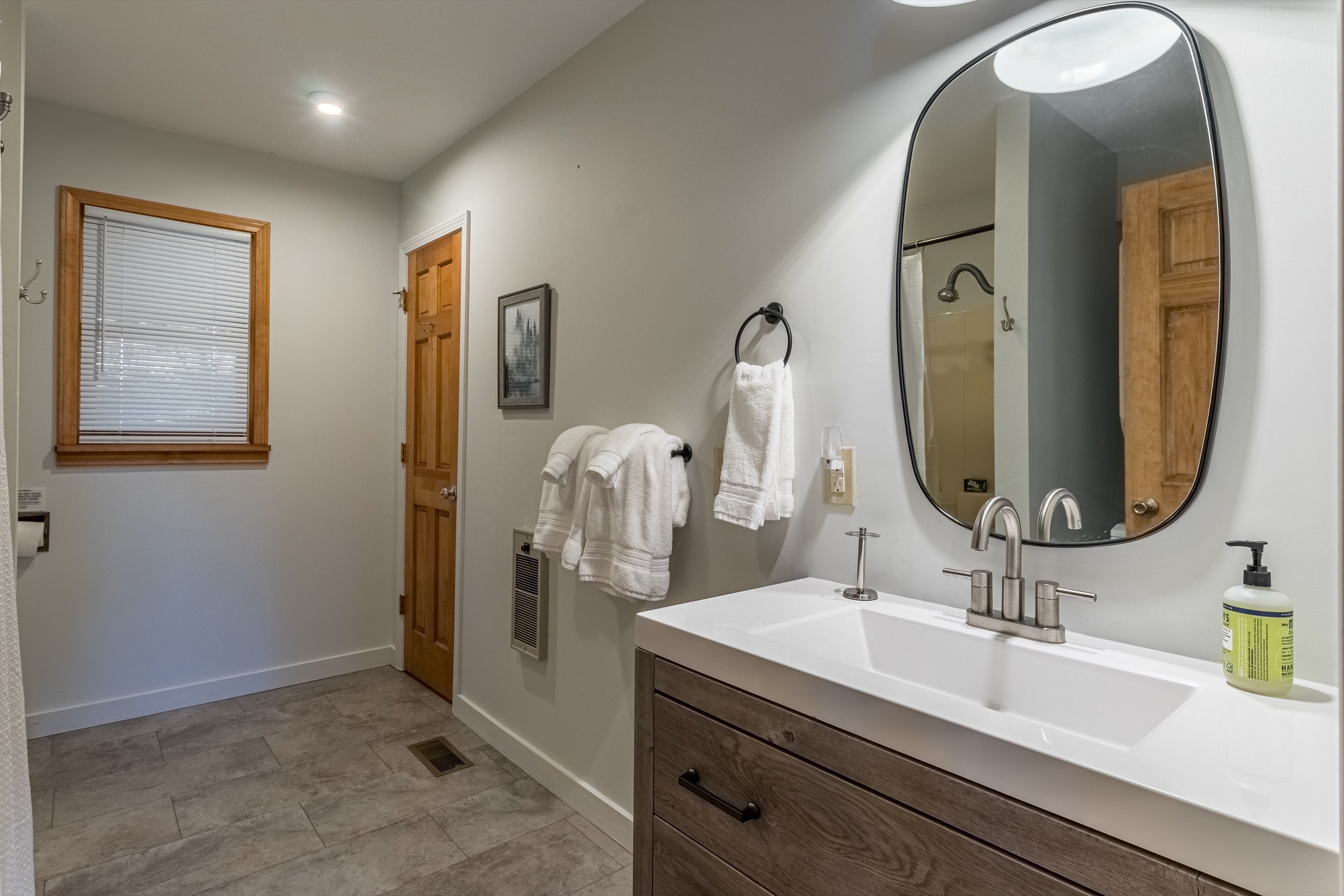 Un bagno con un lavandino bianco, uno specchio grande, mobiletti in legno e un portascopino con asciugamani.