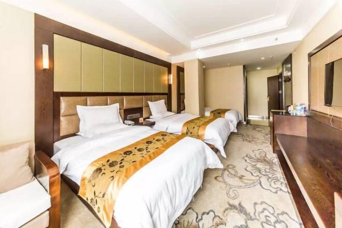A hotel room with two beds, a large mirror, and a wooden headboard.