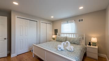 Un dormitorio con una cama, dos mesitas de noche, una ventana con cortinas y una puerta.