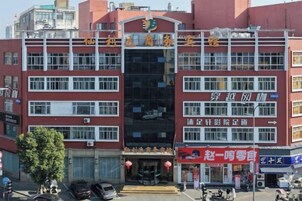 Um edifício de vários andares com placas indicando que é um hotel. Há várias janelas em cada andar, e a entrada possui uma área coberta com uma placa acima.