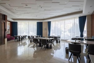 Comedor de hotel con mesas y sillas, ventanas amplias con cortinas y un piso pulido.