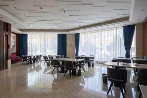 A hotel dining area with tables and chairs, large windows with curtains, and a polished floor. - Xianlida Business Hotel (Rui'an)