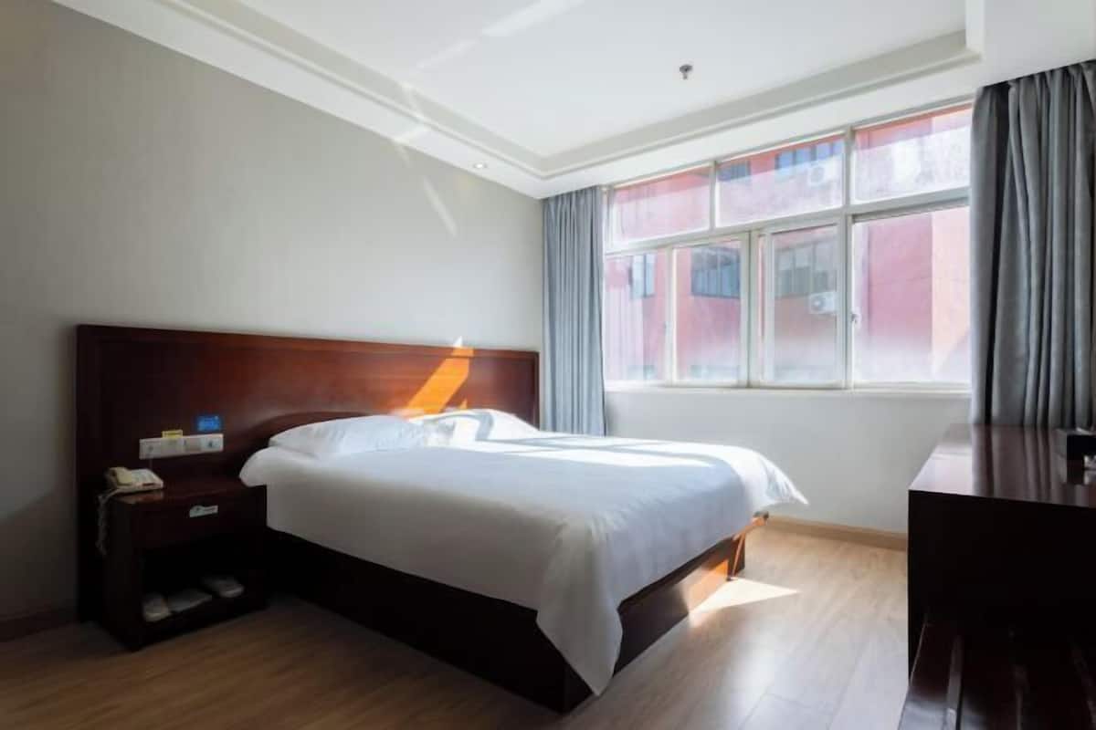Una habitación de hotel con una cama de madera, una mesita de noche con teléfono, un escritorio y una ventana con cortinas.