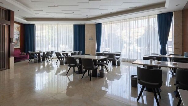 Uma sala de conferências ampla, com várias mesas e cadeiras, grandes janelas com cortinas azuis e piso lustroso.