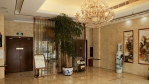 Um saguão com um candelabro, um vaso de planta, um vaso e obras de arte nas paredes.