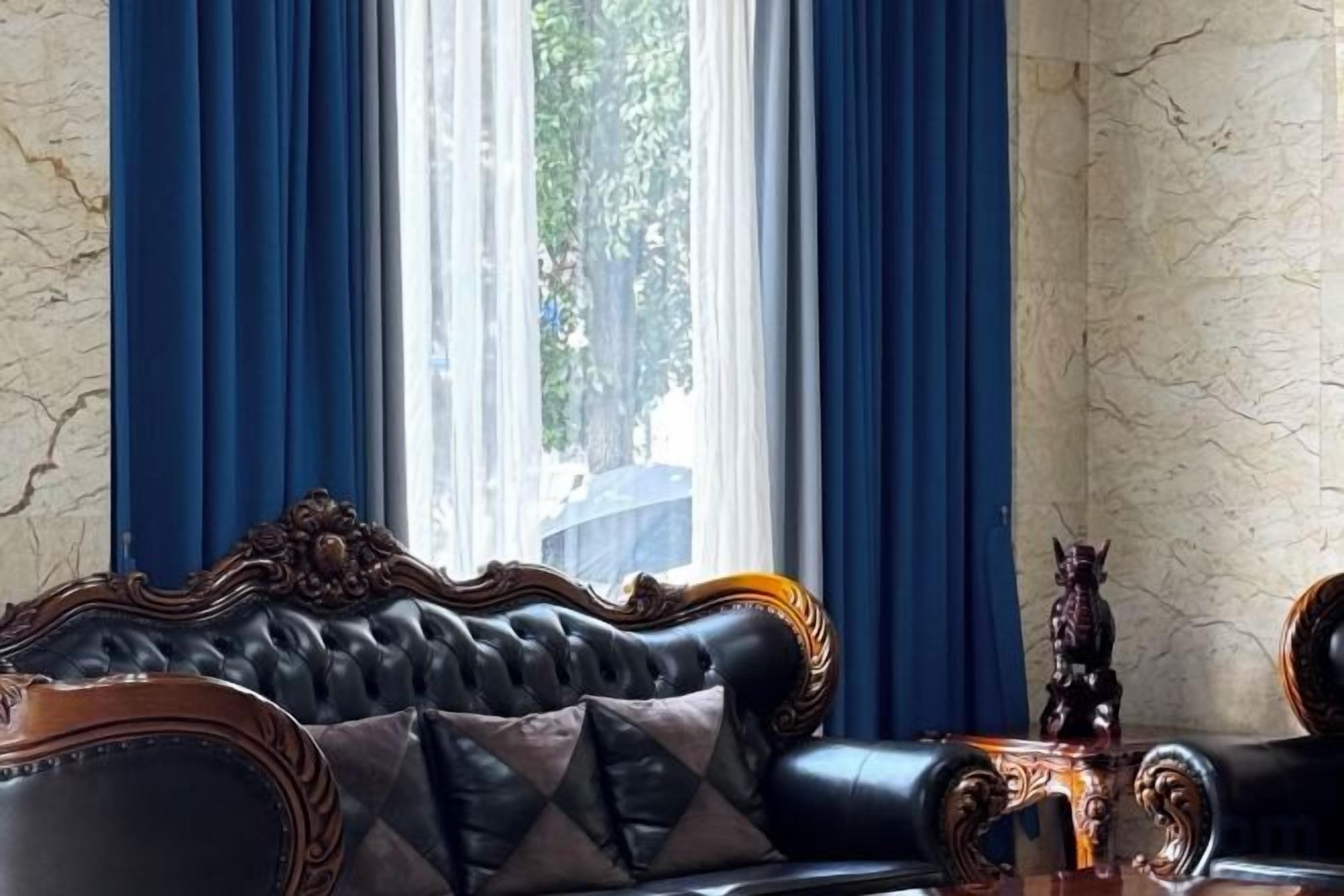 A room with a leather sofa, a decorative table, and a view through a window with blue curtains.