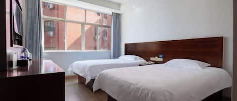 A hotel room with two beds, a desk, and a window with a view of buildings.