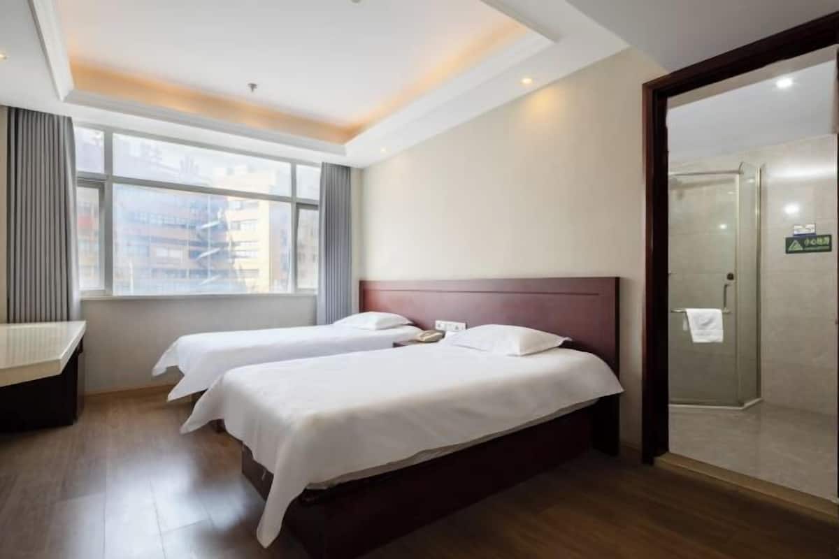 Habitación de hotel con dos camas, un escritorio, una ventana con cortinas y una puerta de ducha de vidrio.