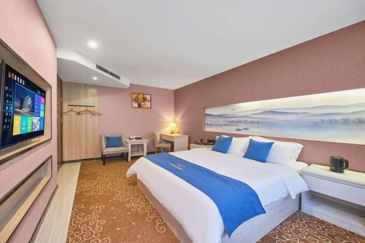 A hotel room with a large bed, a desk, a chair, a TV, and a painting on the wall.