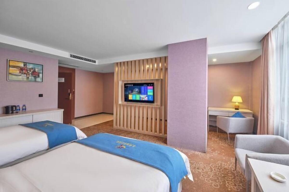 A hotel room with two beds, a desk, a TV, and a lamp.