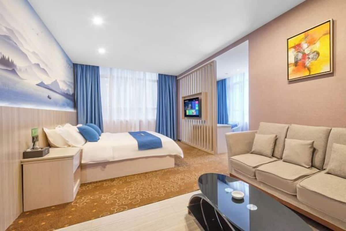 A hotel room with a bed, a sofa, a TV, and a painting on the wall.