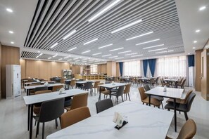 A spacious dining area with multiple tables and chairs, a modern ceiling design, and a kitchen area in the background. - Laiyue Hotel (Huidong)