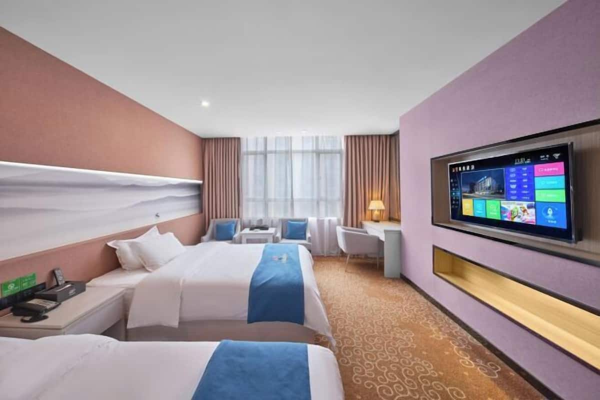 A hotel room with two beds, a desk, a chair, a TV, and a window with curtains.